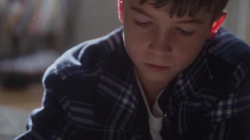 A young boy gazes downward with a contemplative expression in soft indoor light