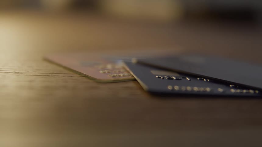 A close shallow depth of field view shows two credit cards resting on a wooden surface with soft light reflecting off their surfaces