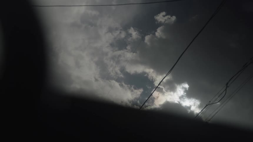 He video shows a view of the sky largely obscured by a dark foreground element possibly a silhouette of a structure or obstructionthe visible portion of the sky is dominated by dark dramatic clouds with patches of brighter whitegray cloudsa sli