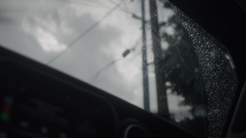 The video shows a view from inside a vehicle on a rainy or recently rained daythe view through the window is dominated by a grey overcast sky with raindrops visible on the side window glass giving the scene a somber or muted atmosphereoutside a