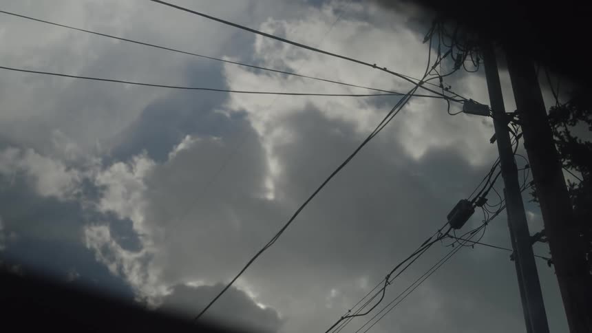 A windshield wiper sweeps steadily across the glass of a stationary vehicle framing a view of dark storm clouds drifting behind silhouetted power lines