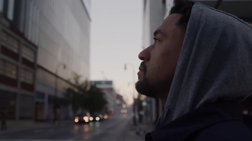 Man standing outside of downtown buildings looking up as cars move on the street