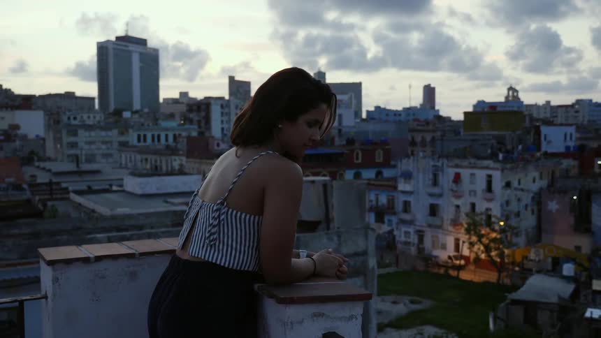 A woman stands on a rooftop overlooking a city