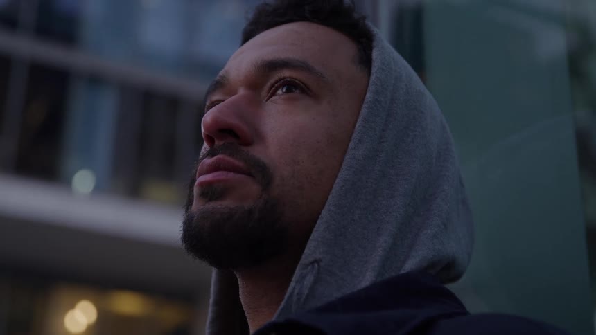 Hooded man looks at buildings around him in an urban setting