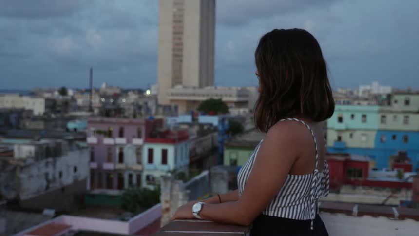 A woman stands on a roof top and looks out at the city below