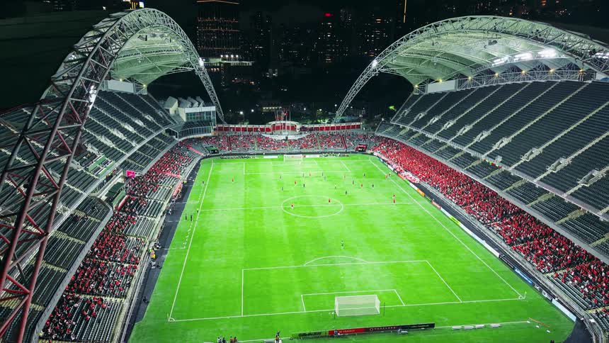 Aerial view of a crowd of people in the bleachers at a soccer stadium watching the players on the field with Dense City Skyline Backdrop