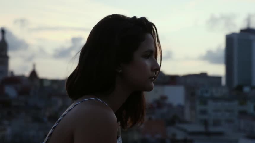 A woman stands on a rooftop overlooking a city