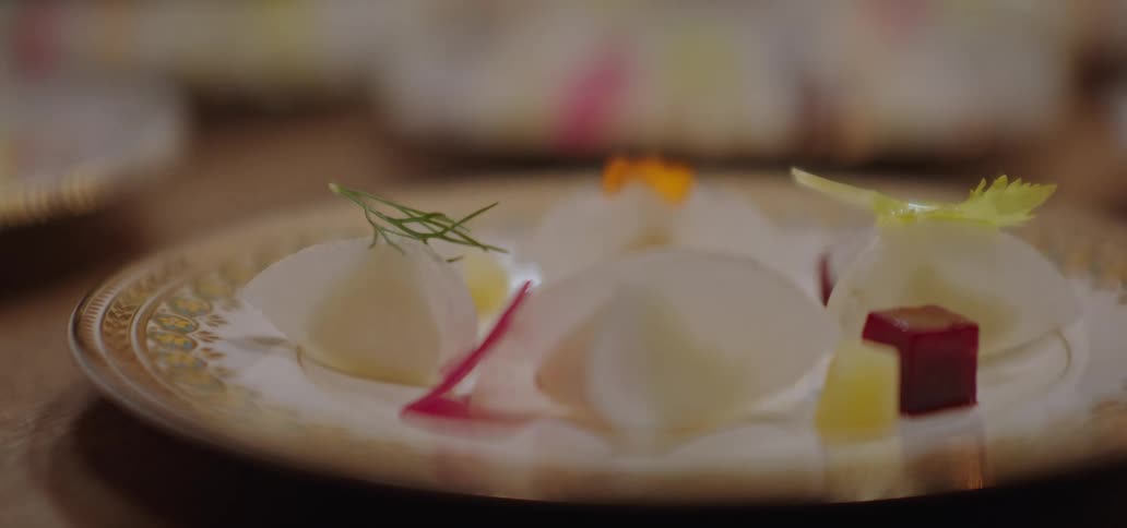 Tongs place a sprig of herb on a decorated plate with small food portions