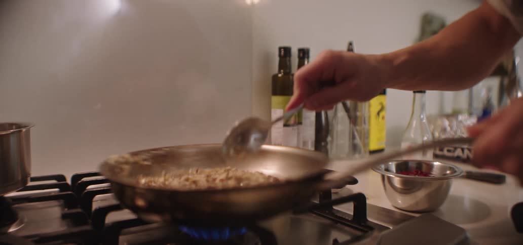 Man stirring food in a skillet in the kitchen turns to look around