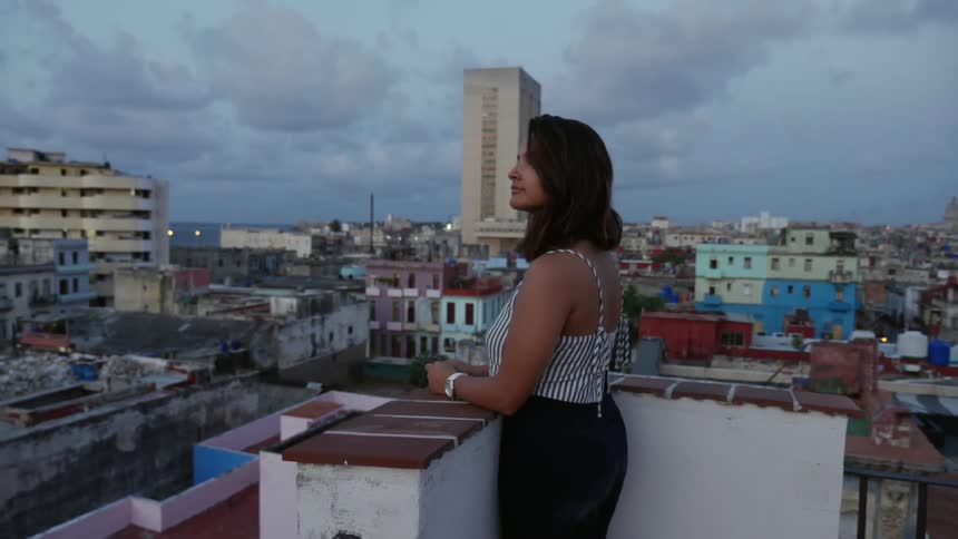 A woman stands on a rooftop overlooking a city