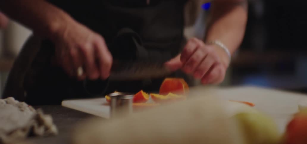 Cook standing in a kitchen slicing an orange