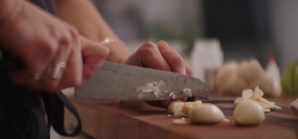 A man uses a knife to quickly slice a piece of garlic on a cutting board