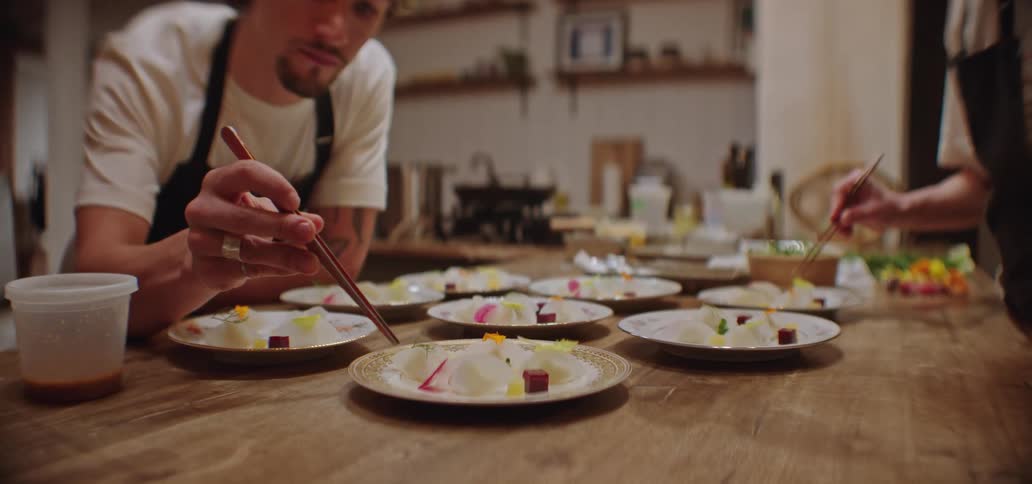 Two young men arranging food on plates with chopsticks on a table