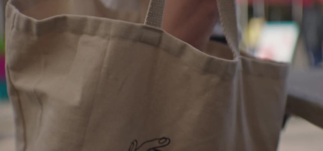 Man places items in a canvas bag at a busy market before walking away during the day