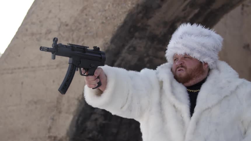 A man in a fur coat loads and shoots a gun