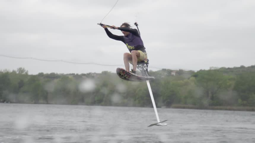 A man sits on a seat attached to a boat and does tricks in the ocean