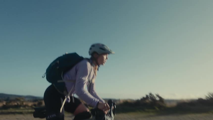 Woman wearing a backpack as she rides a bicycle across rural terrain