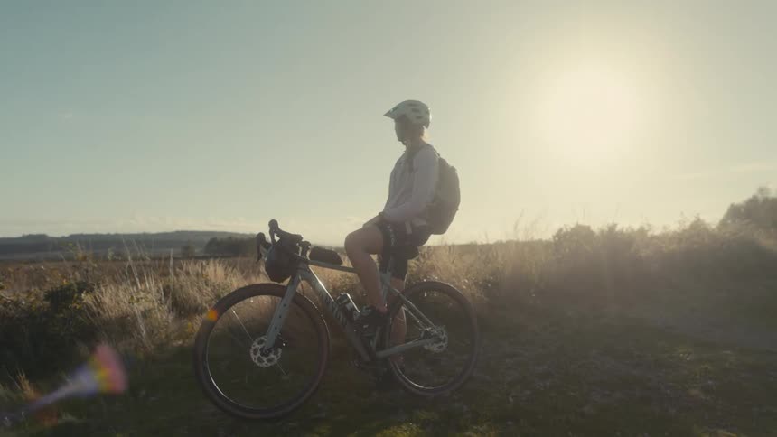 Cyclist standing beside the bike with the low sun on the horizon