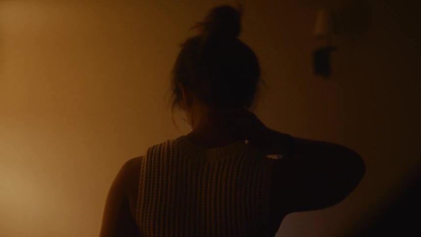 Woman in a dimly lit room rubs her neck