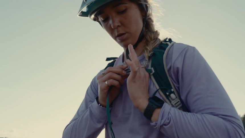 A young blonde woman wearing a helmet is fastening a belt around her waist