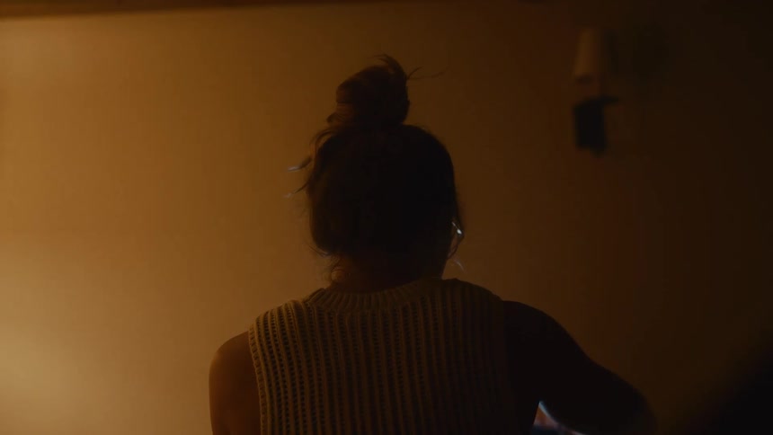 Woman with a bun and glasses is drinking in a room lit by warm light