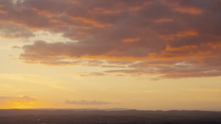 The sun sets near a mountain range with colorful clouds in the sky