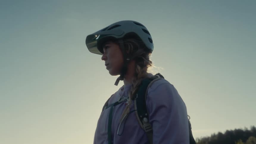Teenage girl sits on her bicycle looking around as the sun shines brightly in the distance