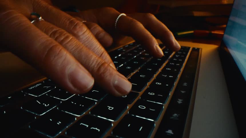 Hands typing on an illuminated laptop keyboard