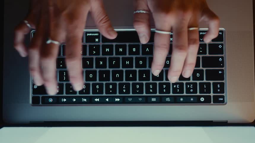 The hands of a person wearing several rings on their fingers typing on a black keyboard