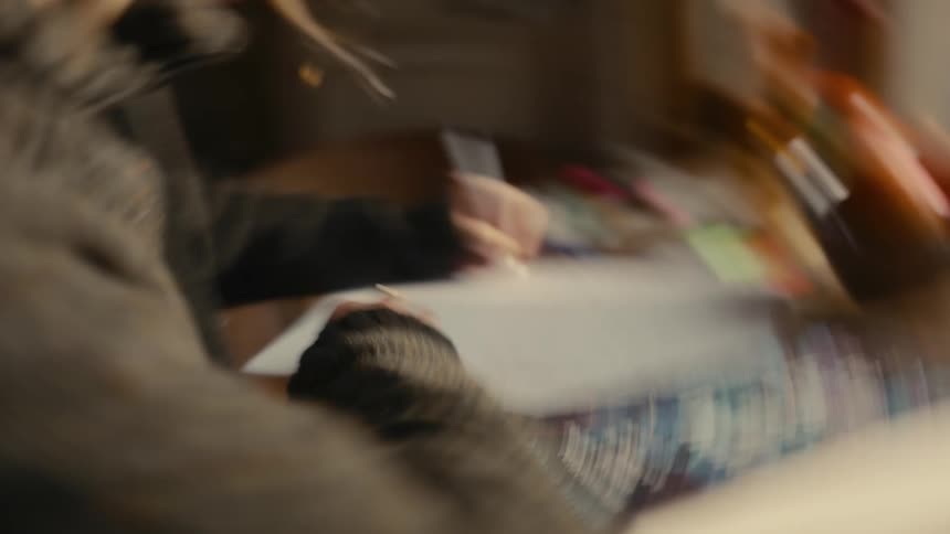 Blonde woman sitting at a table writes on paper during the daytime