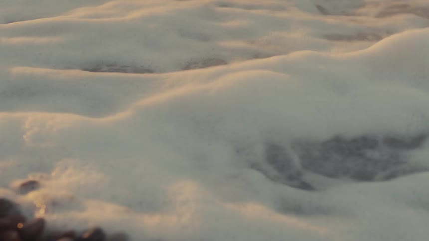 Wave foam washing over beach pebbles