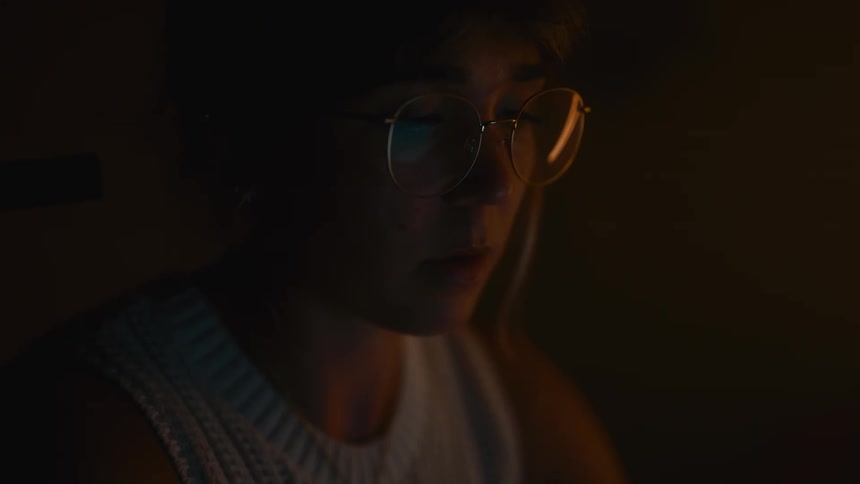 Person wearing glasses looking at a lit screen in a dark room