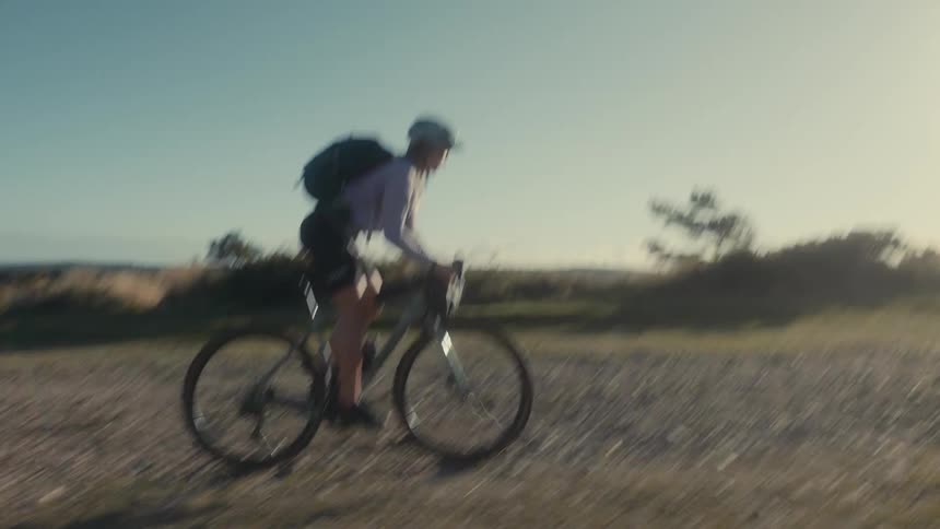 Young woman wearing a backpack rides a bicycle through a rural field