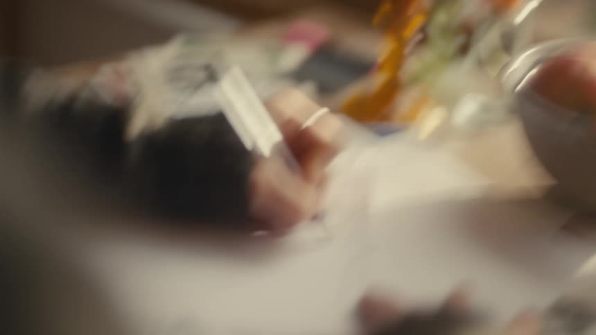 A persons hands using a pen to write on a white sheet of paper that is on a table