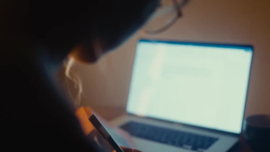 The woman is writing in her notebook by her laptop