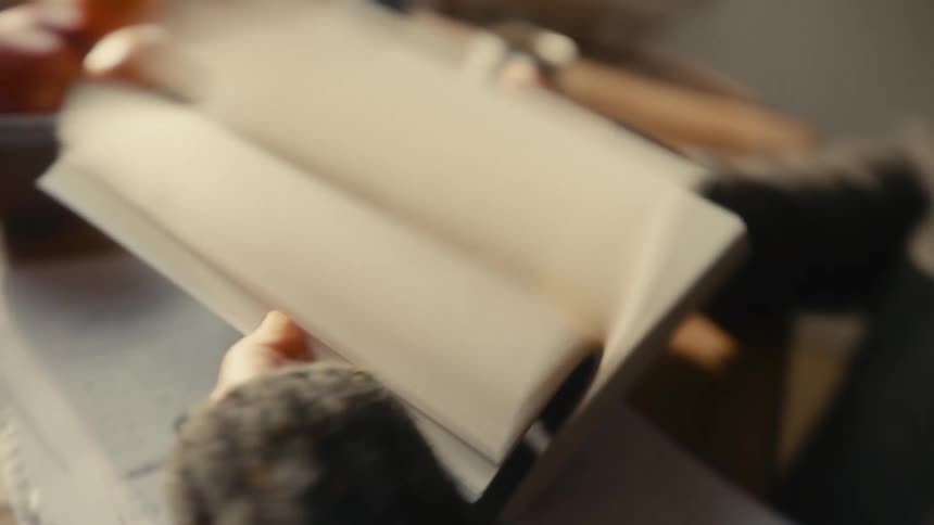 Hands flip through notebook in a reading setting with blurred background