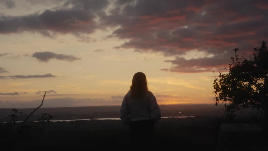The silhouette of a person standing looking at a sunset on the horizon