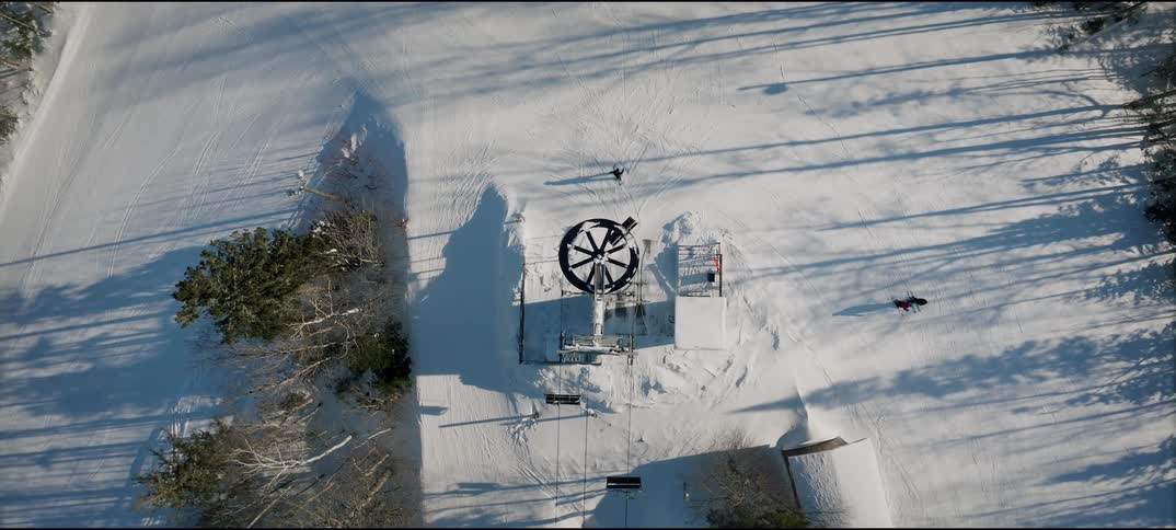Seats on a ski lift move over a snow covered mountain as a skier slides down the slope