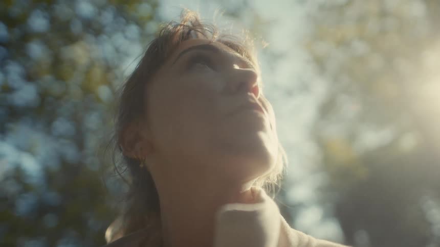 Young adult woman looking around on an area surrounded by trees outdoors during dusk or dawn