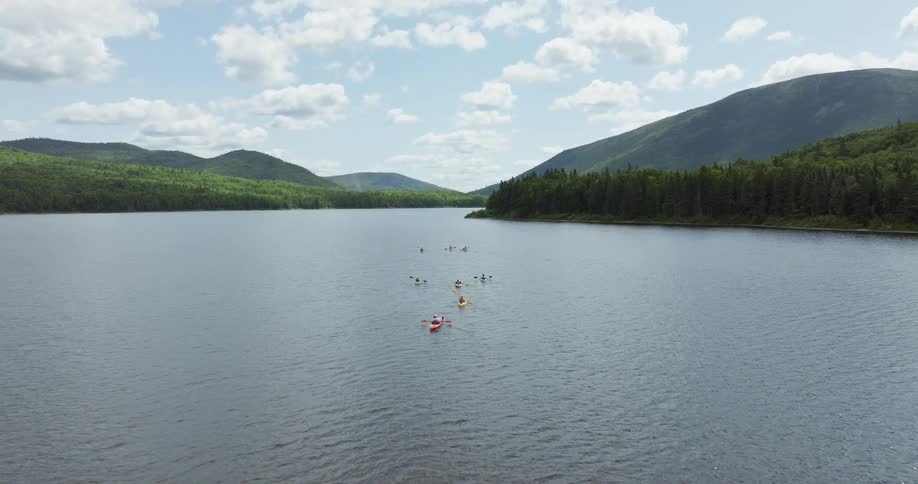 People row kayaks across a river in a forested mountain valley
