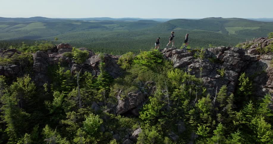Three people walk along a rocky ridge surrounded by dense forest