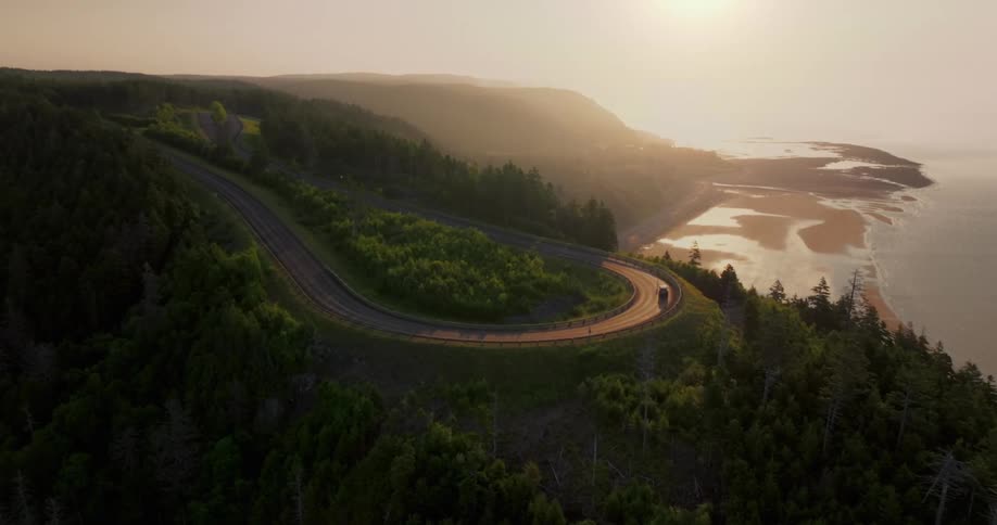 Winding coastal road lit by the low sun over the sea