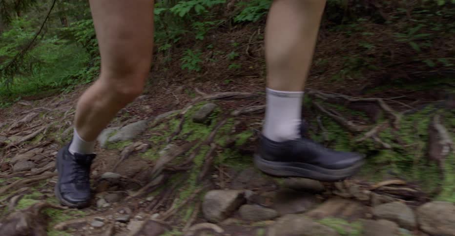 A person jogging up a rocky forest trail at midday wearing sneakers white socks and shorts