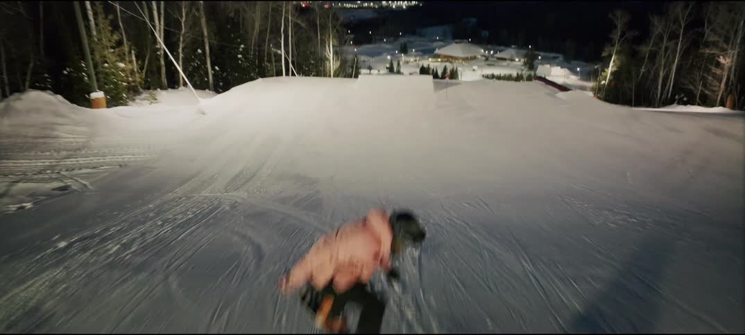 Person in pink jacket descends snowcovered slope under night lighting