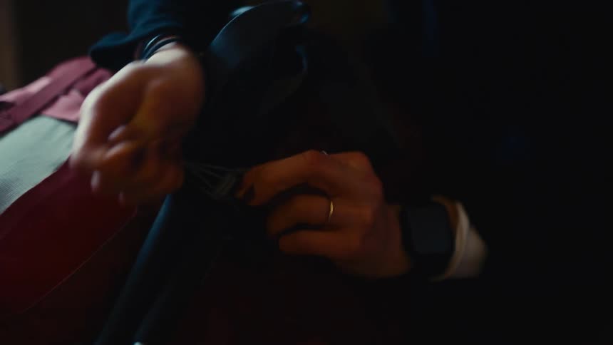 Hands adjusting the strap of a red backpack on a dark surface