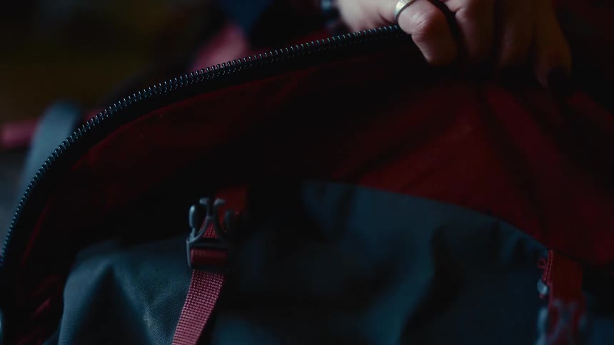 Hand opens zipper of red and black backpack