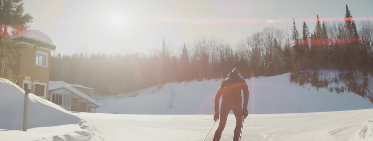 A cross country skier glides down a sunlit groomed winter trail