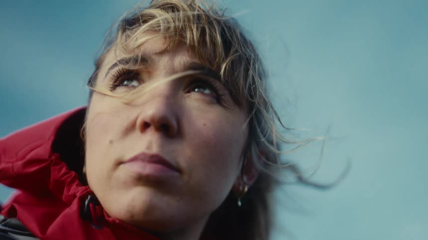 A woman in a red jacket looks skyward as the wind blows through her hair