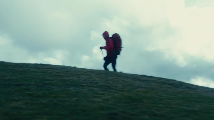 A person wearing a coat and a large backpack is walking up a hill