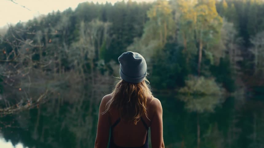 Woman wearing a beanie looking at the lake surrounded by forest